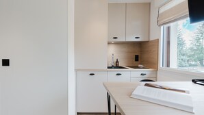 A modern kitchen with white cabinets, a wooden backsplash, and a window with a view of trees. - 102 - Appart'Hôtel Neostelia-Annecy (Annecy)