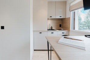 Eine moderne Küche mit weißen Schränken, einer Holzrückwand und einem Fenster mit Blick auf Bäume.