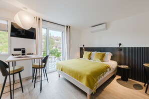 Ein modernes Schlafzimmer mit einem Bett, einem Schreibtisch mit Stühlen, einem Fernseher und einem Fenster mit Blick ins Freie.