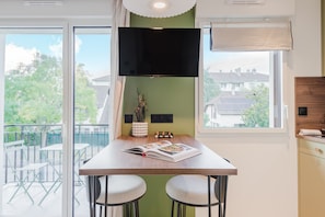A modern kitchen with a large window, a flat-screen TV, and a dining area with two stools. - 103 - Appart'Hôtel Neostelia-Annecy (Annecy)