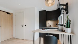 A modern kitchen with a dining area, featuring a wooden door, a white door, a black cabinet, a white potted plant, and a magazine on the table.
