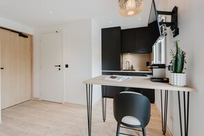 Una cocina moderna con comedor, que incluye una puerta de madera, una puerta blanca, un armario negro, una planta blanca en maceta y una revista sobre la mesa.