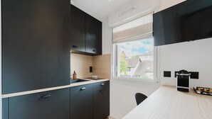 A modern kitchen with dark cabinetry, a wooden countertop, and a window with a view of buildings outside.