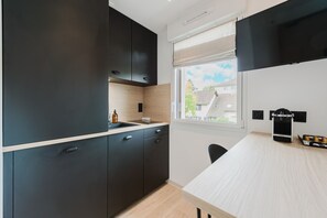 Una cocina moderna con armarios oscuros, encimera de madera y ventana con vistas a edificios.