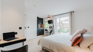 A modern hotel room with a bed, a desk with a laptop, a chair, and a balcony with a view.