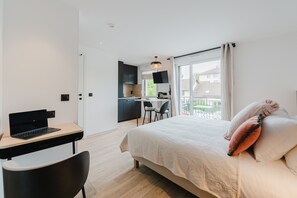 Una habitación de hotel moderna con una cama, un escritorio con una computadora portátil, una silla y un balcón con vistas.