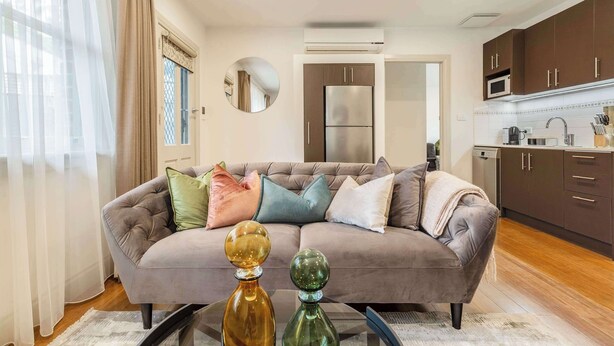 A living room with a sofa, a coffee table, and a kitchen area with cabinets and appliances. - Pet-friendly guesthouse with garden and playground (Ivanhoe)