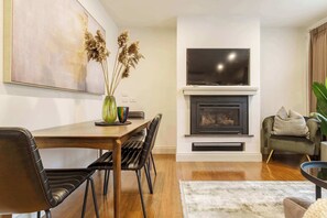 Uma sala de estar moderna com lareira, televisão de tela plana e um espaço de jantar com cadeiras e mesa.