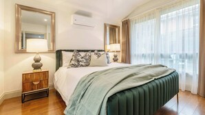 A hotel room with a bed, two bedside tables with lamps, a mirror, an air conditioning unit, and a large window with curtains. - Pet-friendly guesthouse with garden and playground (Ivanhoe)