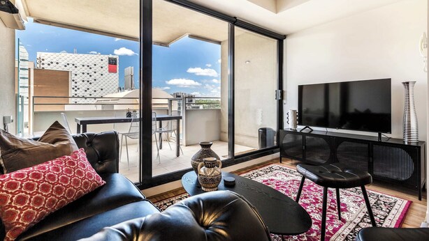Una sala moderna con sofá, televisor y vistas de la ciudad a través de amplias ventanas.