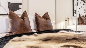 Una cama con una manta de piel sintética, un espejo que refleja una cama con almohadas y una obra de arte abstracta en la pared.