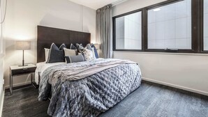 Ein modernes Hotelzimmer mit einem großen Bett, einem Nachttisch, einer Lampe und einem großen Fenster mit Vorhängen.