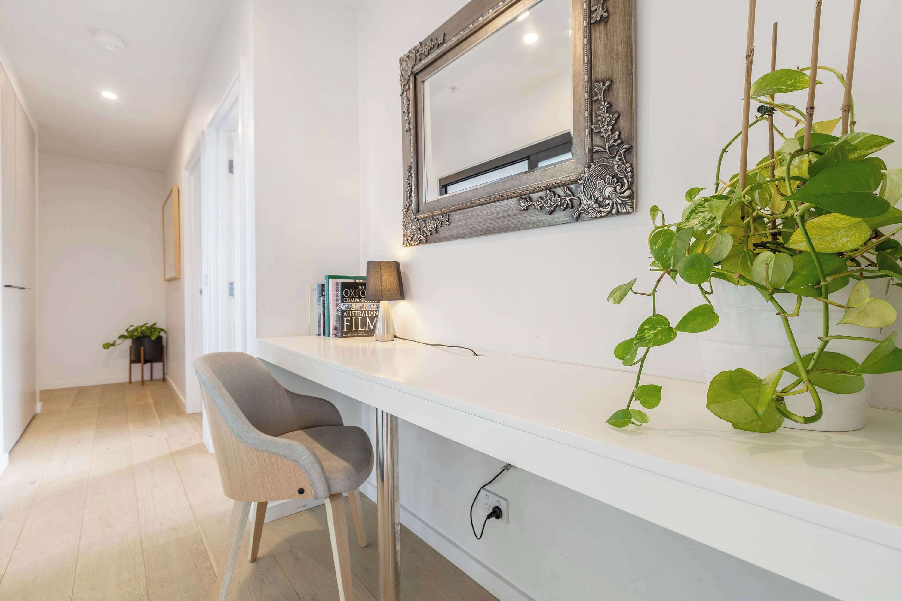 A modern interior with a white desk, a chair, a mirror, and a potted plant.