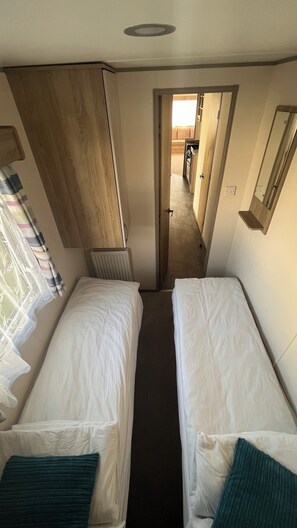 A narrow room with two single beds, a wooden wardrobe, a radiator, and a mirror on the wall.