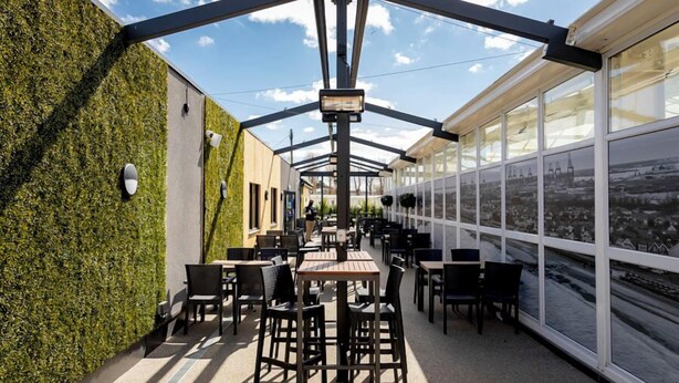 An outdoor patio with tables and chairs, a glass enclosure, and a view of the city. - Rc 39 (Felixstowe)