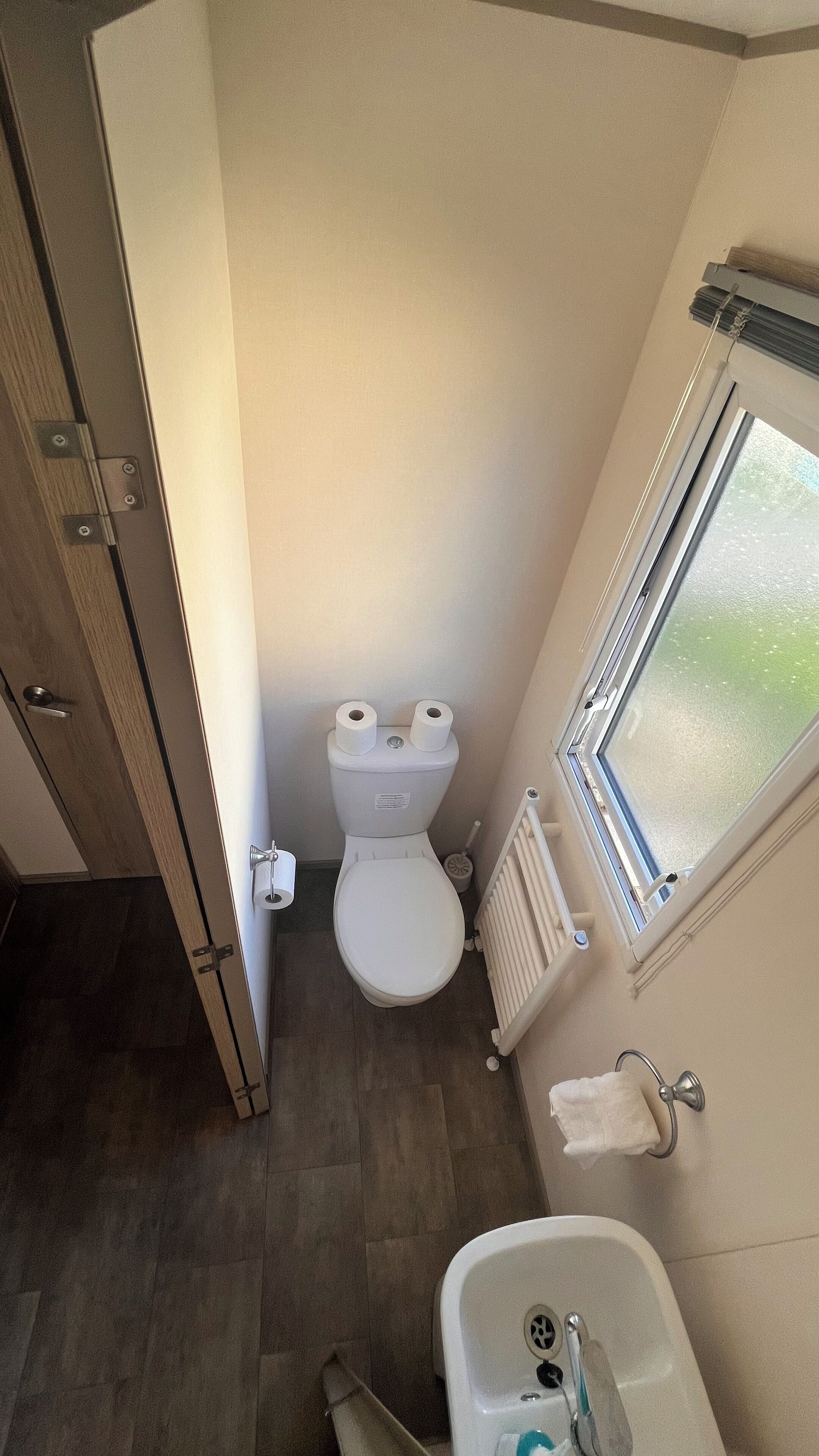 A compact bathroom with a toilet, a small sink, and a window.