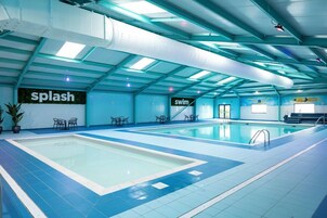 Piscina interna com sinalização clara para áreas de 'splash' e 'swim', com revestimento de azulejos azuis e equipada com assentos e uma escada.