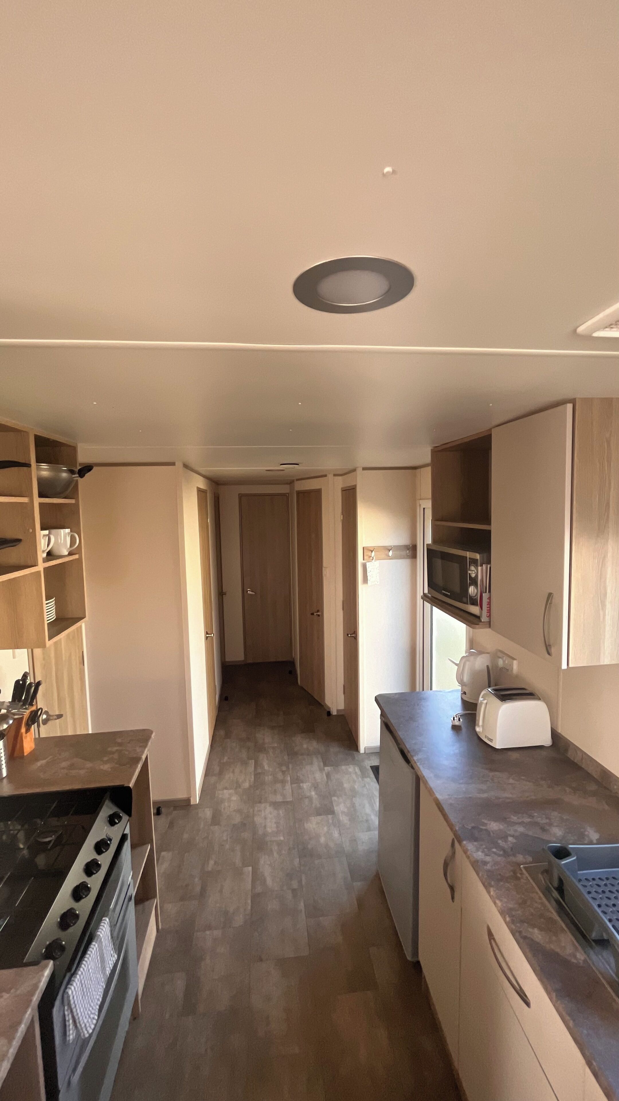 A narrow kitchen with a stove, oven, microwave, and a toaster. There are wooden cabinets and a countertop.