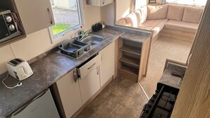 A compact kitchen with a small refrigerator, a sink, and a stove. There is a window providing natural light and a view of the outside. - Rc 39 (Felixstowe)