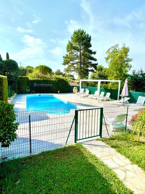 A swimming pool with a fenced area, lounge chairs, and a pergola with umbrellas.