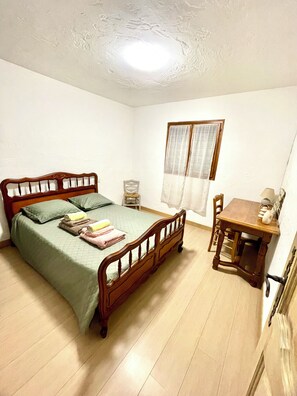 A bedroom with a wooden bed, a small table, a chair, and a window with curtains.