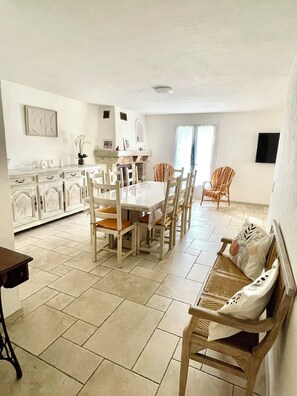 A dining area with a table and chairs, a sofa, a fireplace, and a kitchen in the background.