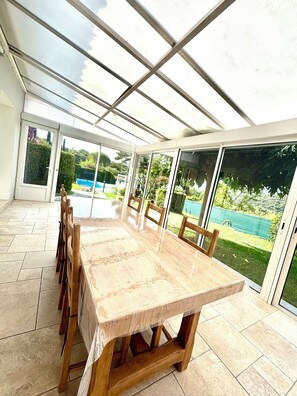 A conservatory with a large table and chairs, glass doors, and a view of a garden.