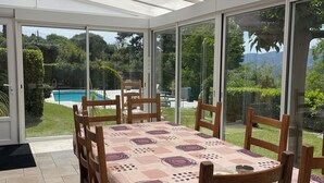 Ein Wintergarten mit Blick auf einen Pool, Holzstühle und ein Tisch mit gemustertem Tischlauf.