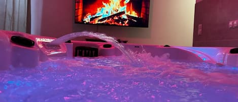 A hot tub with water jets and a television displaying a fireplace scene in the background.