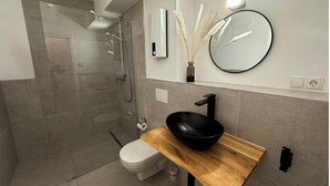 A modern bathroom with a glass-enclosed shower, a wooden vanity with a black sink, and a round mirror. - Rheinmosel Glück Wellness (Koblenz)