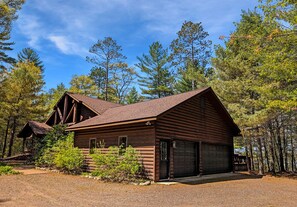Une cabane rustique en rondins de bois, dotée d’un garage, et entourée d’une forêt dense.
