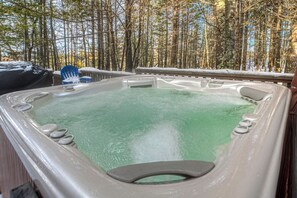 Un bain à remous entouré d’une terrasse en bois, avec une forêt en arrière-plan.