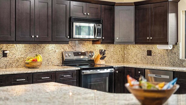 A kitchen with dark wood cabinets, a stainless steel microwave, a stove, and granite countertops.