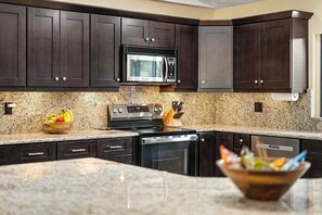 Una cocina con gabinetes de madera oscura, microondas de acero inoxidable, estufa y encimeras de granito.