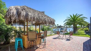 An outdoor patio with a thatched umbrella, wooden bar, and seating area.