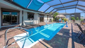 A swimming pool with a glass enclosure, surrounded by lounge chairs and a covered patio area.