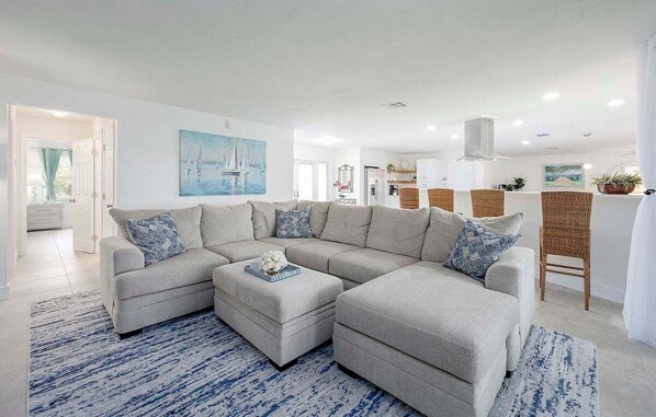 A modern living room with a sectional sofa, a coffee table, and a dining area with wicker chairs.