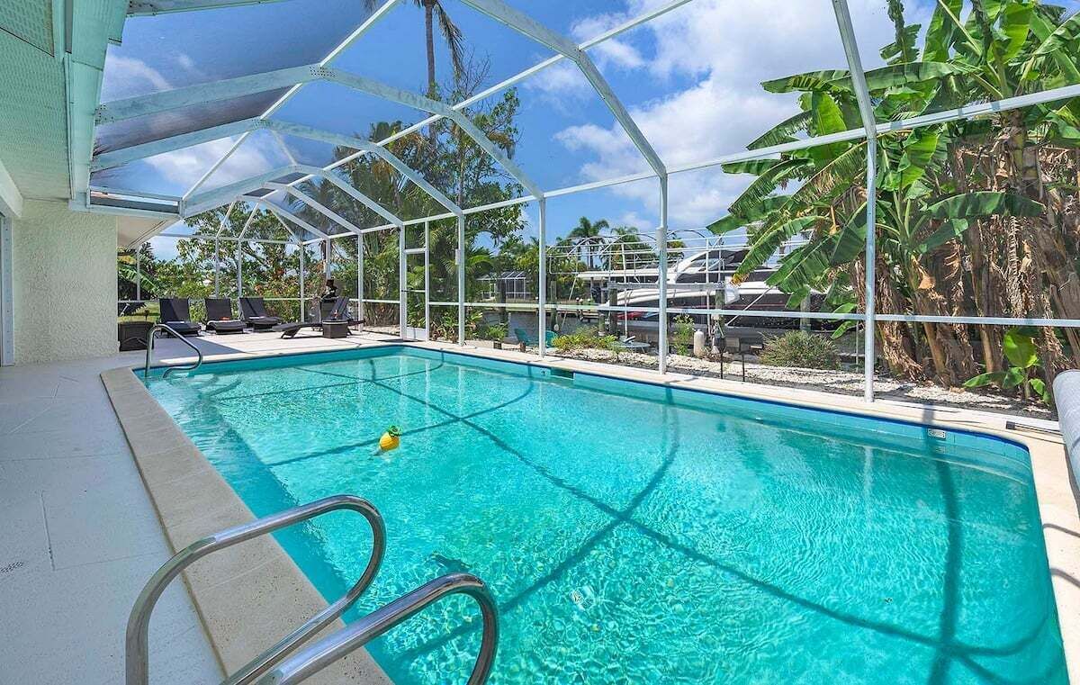 A pool with clear blue water, surrounded by a glass enclosure, and a few lounge chairs.