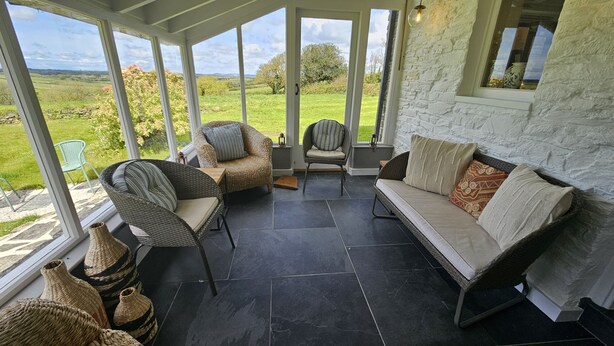 A covered patio area with wicker furniture, a stone wall, and a view of the countryside.