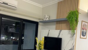 Ein modernes Wohnzimmer mit einem Flachbildfernseher an einer Marmorwand, einer eingebauten Bank mit Telefon und einer kleinen Pflanze, und einer Glastür, die zu einem Außenbereich führt.