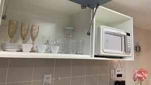 Eine Küche mit einem weißen Regal, das Glaswaren, eine Mikrowelle und eine Steckdose beherbergt.