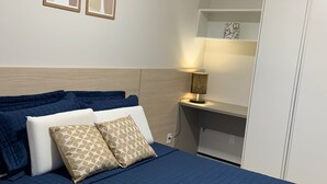 Ein ordentlich bezogenes Bett mit einer blauen Steudecke, zwei Kissen und einer Nachttischlampe.
