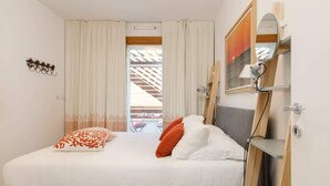 Een slaapkamer met een bed, kussens, een nachtkastje, een spiegel en een raam met gordijnen.