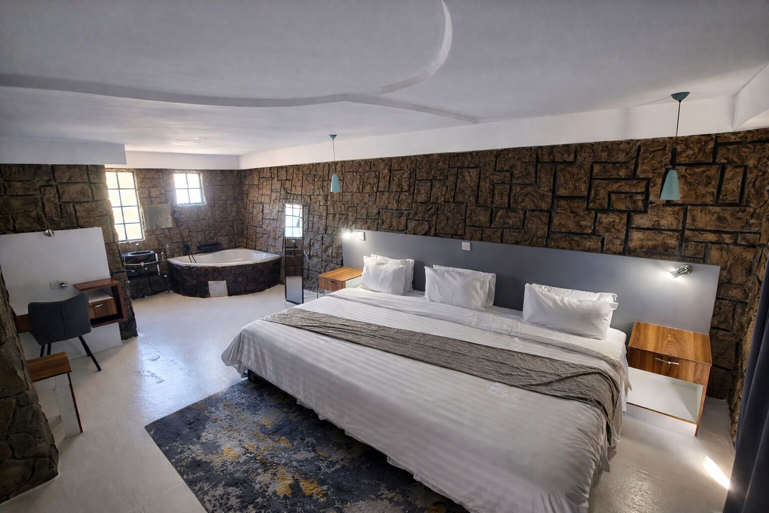 Un dormitorio moderno con una cama grande, pared de piedra, bañera y escritorio.
