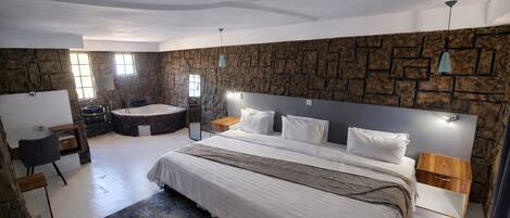 Un dormitorio moderno con una cama grande, pared de piedra, bañera y escritorio.