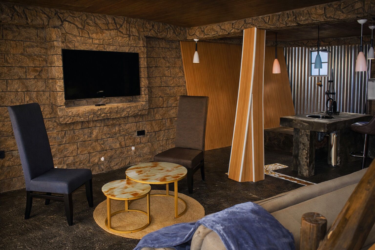 Un rincón de descanso acogedor con pared de piedra, televisor de pantalla plana, zona de bar y disposición de asientos que incluye un sofá y dos mesas redondas.