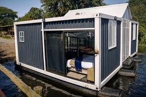 Una casa flotante con un amplio ventanal corredera, una pequeña terraza y una ventana.