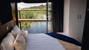 Ein Schlafzimmer mit einem großen Bett, einem Holzkopfteil und Blick auf ein Gewässer durch ein Fenster.