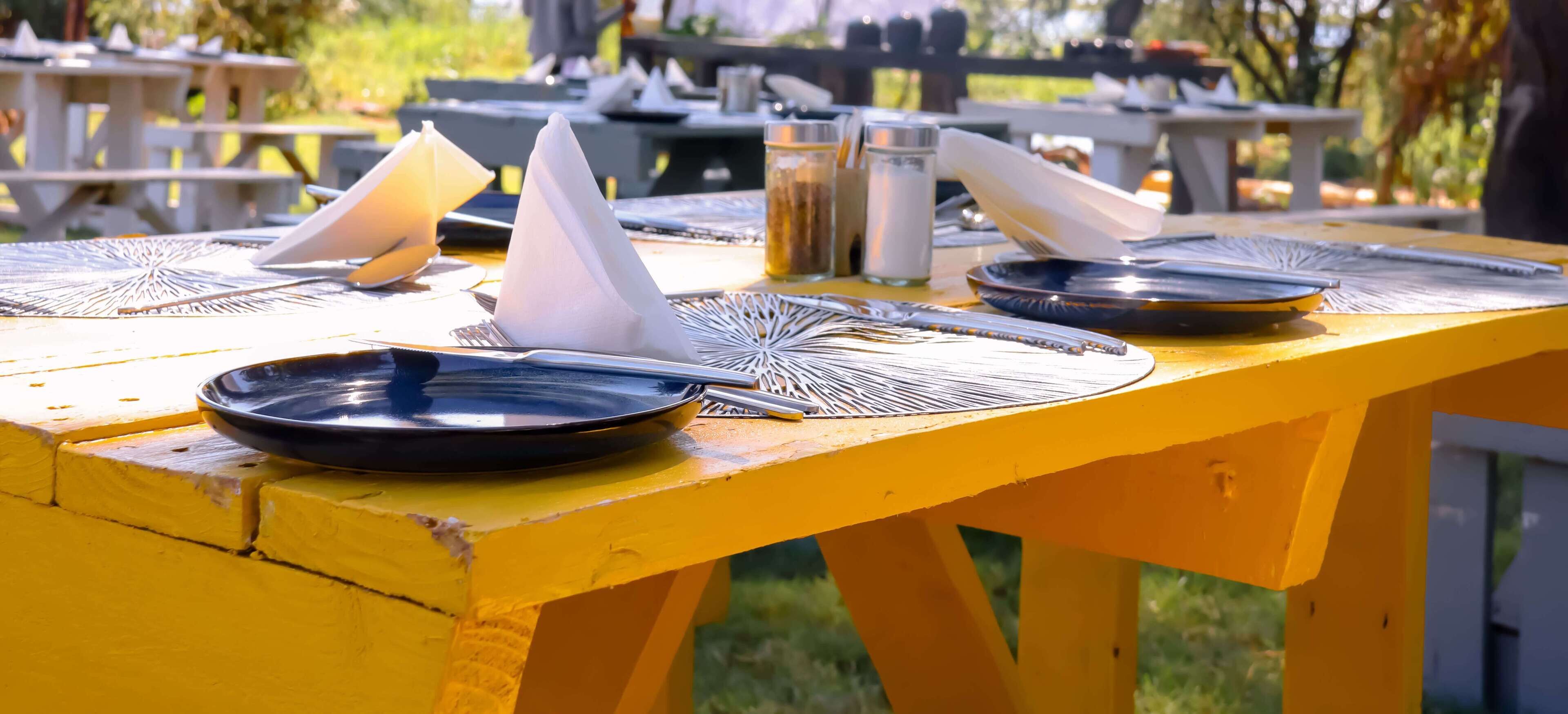 A yellow picnic table with a black plate, a folded napkin, and a fork.