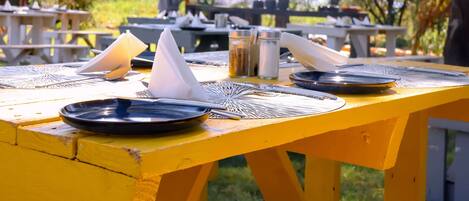 A yellow picnic table with a black plate, a folded napkin, and a fork.